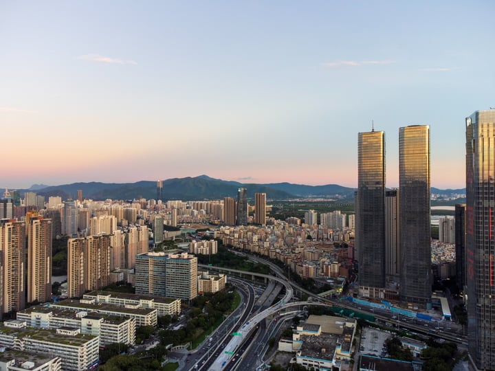 A cityscape with tall buildings, a river, and mountains in the background.