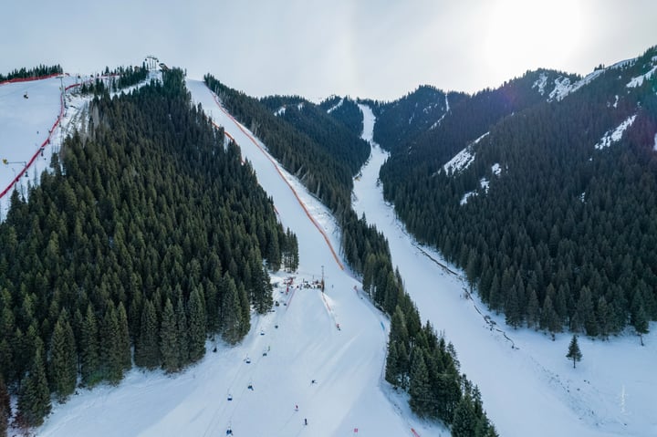 A snowy mountain slope with a red fence, a ski lift, and a vast landscape with snow-covered mountains and trees.