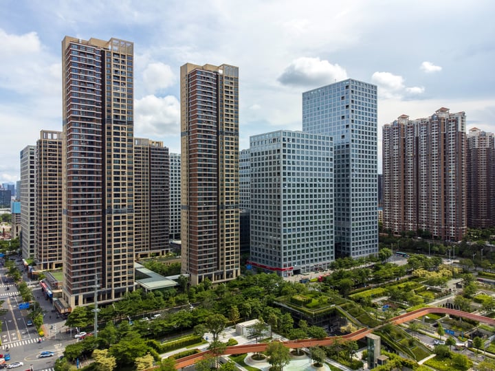 A bustling cityscape with tall buildings, a park, and a road, all under a clear blue sky.