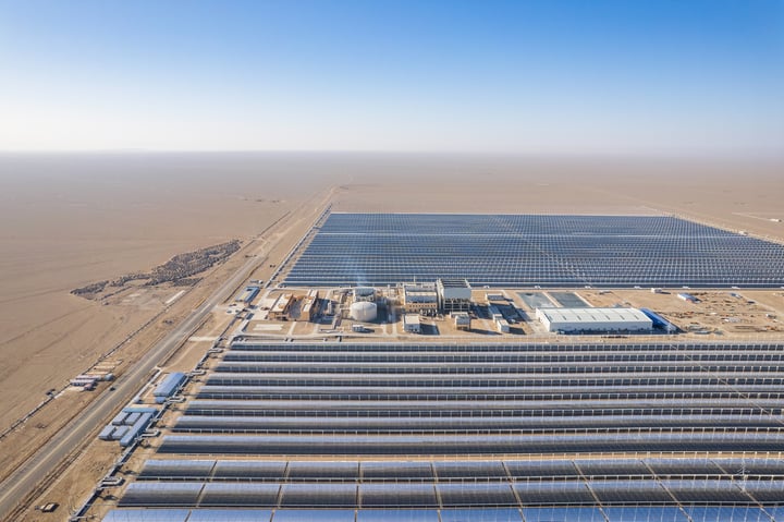 An aerial view of a large solar farm with rows of solar panels in a desert-like environment.