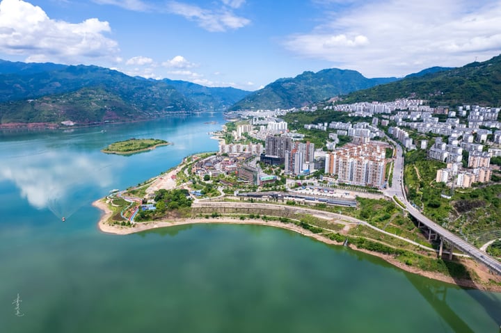 An aerial view of a city nestled between mountains, with a large body of water in the foreground and a cityscape in the background.