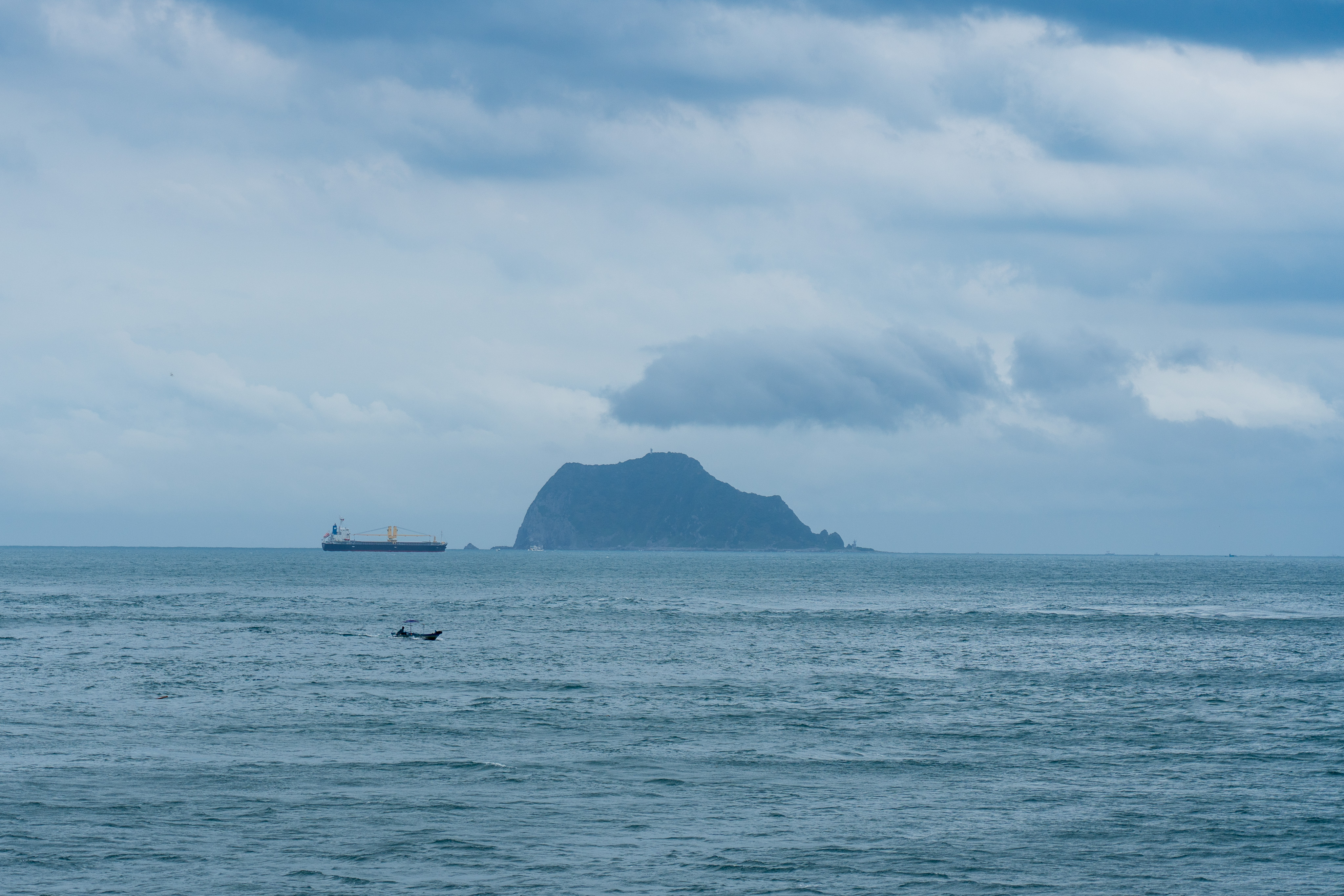 A large island with a dark green mountain and a small boat in the distance.