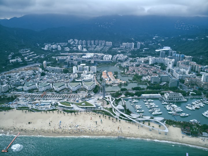 An aerial view of a bustling city with a large body of water filled with boats, surrounded by mountains and a large cityscape.