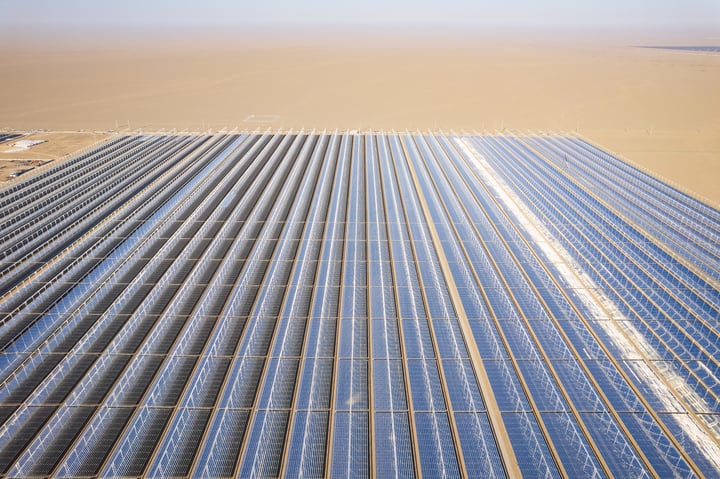 An aerial view of a large solar farm with rows of solar panels in a desert-like environment.