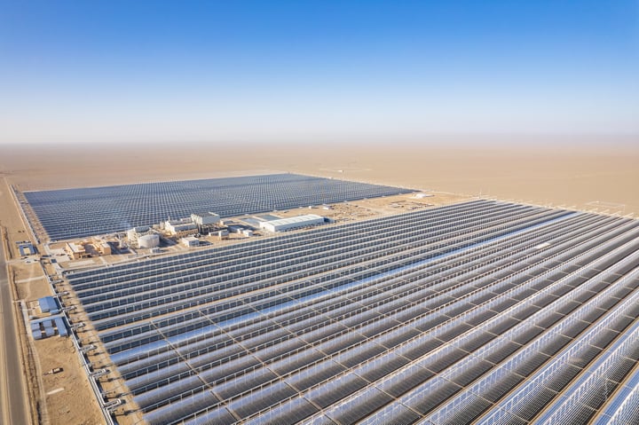 An aerial view of a large solar farm with rows of solar panels in a desert-like environment.