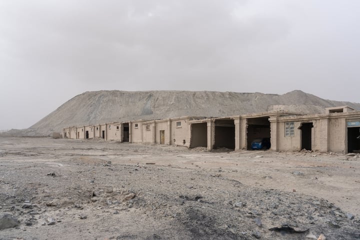 A desolate desert landscape with a row of old, weathered buildings, a large hill, and a cloudy sky.