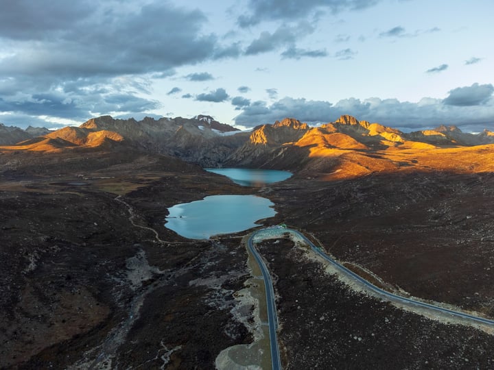 An aerial view of a mountainous landscape with a large lake, surrounded by rugged mountains and a winding road.