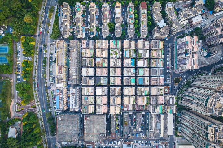 An aerial view of a city with a grid-like layout of buildings, roads, and parks, surrounded by greenery.