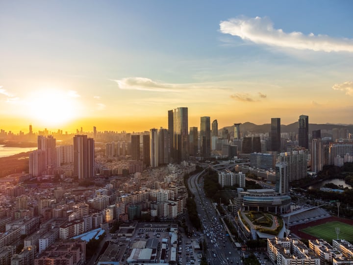 An aerial view of a bustling city at sunset, with tall buildings and a river in the background.