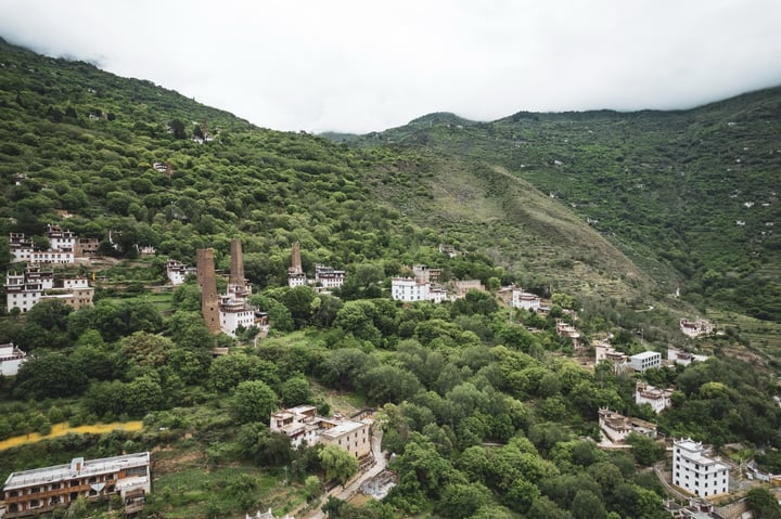 An aerial view of a mountainous area with a mix of old and new buildings, surrounded by lush greenery.