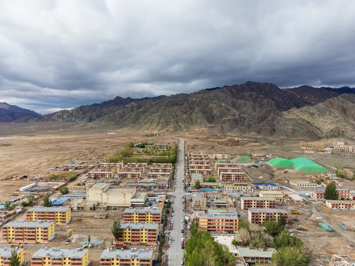 A mountainous landscape with a city in the center, surrounded by mountains and a cloudy sky.