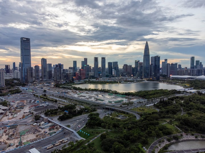 Aerial view of a city skyline with tall buildings, a river, and a bridge, with a cloudy sky.