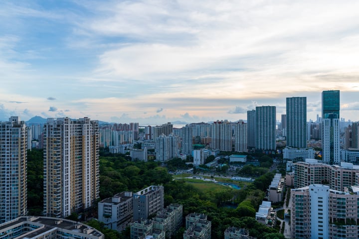 A cityscape with tall buildings, a park, and a blue sky with clouds.