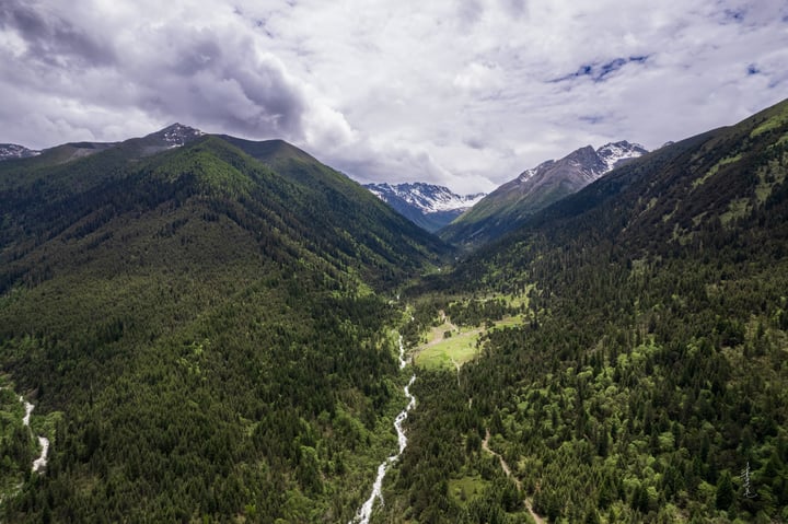 An aerial view of a lush green valley surrounded by snow-capped mountains, with a winding river running through it.
