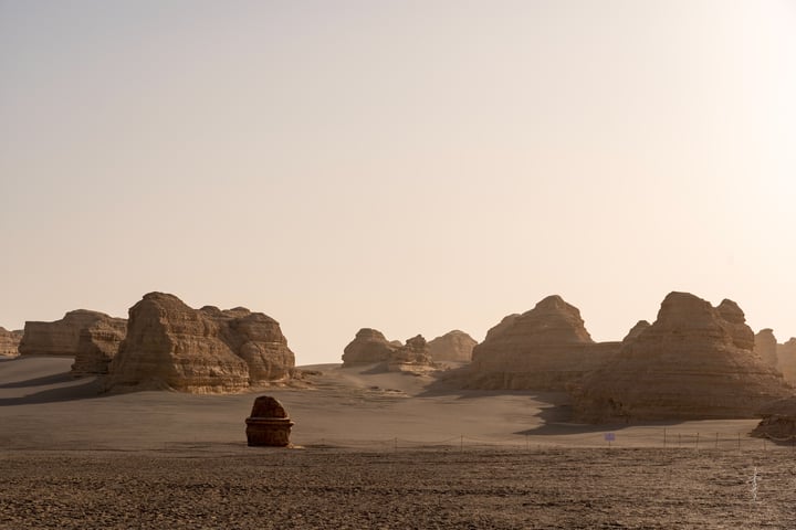 A desert landscape features sand dunes, a red barrel, and a pale blue sky.