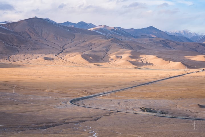 A vast, barren landscape with a winding river, mountains, and a few wind turbines in the distance.