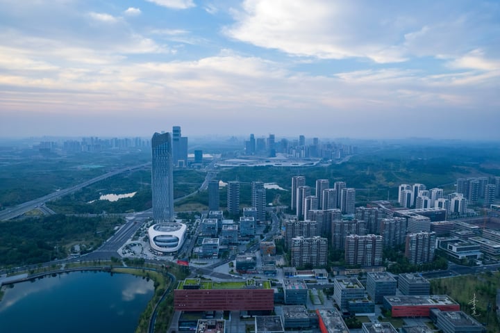 An aerial view of a city with tall buildings, a river, and a park, with a blue sky and clouds.