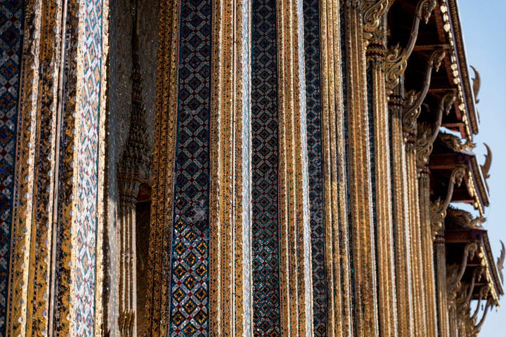 A close-up view of a temple's ornate columns, adorned with intricate gold patterns, is captured against a clear blue sky.