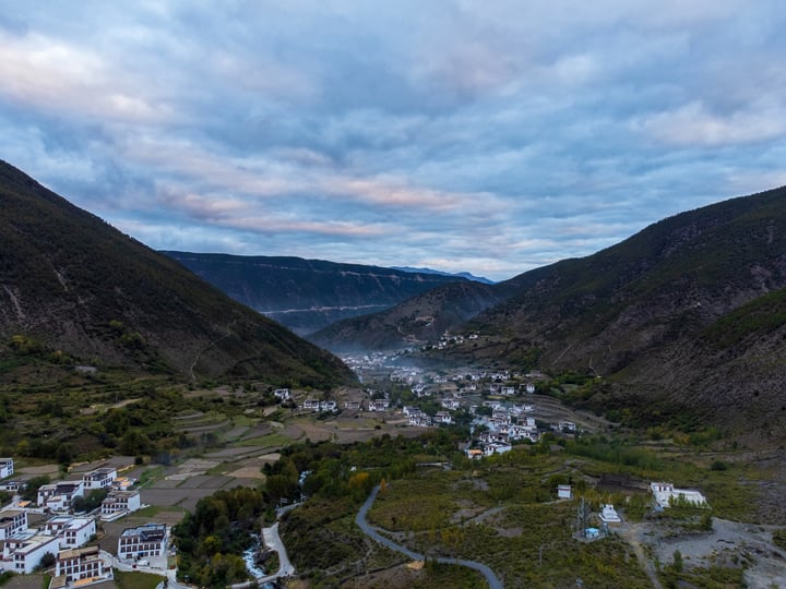A picturesque valley with a small town nestled between mountains, surrounded by lush greenery and a winding river.