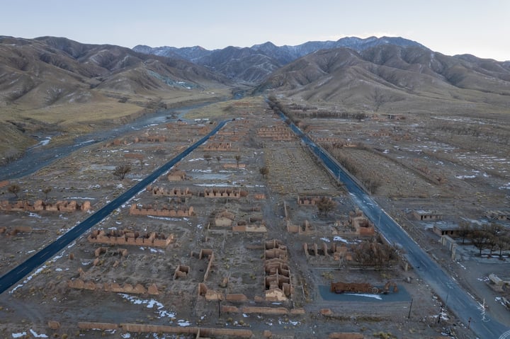 An aerial view of a desert landscape with a road, buildings, and mountains in the background.