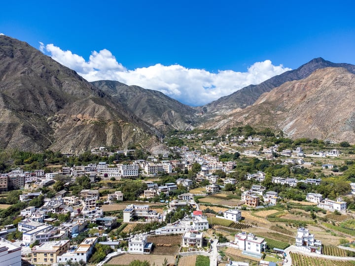 A picturesque mountain town with white buildings, green fields, and a clear blue sky.
