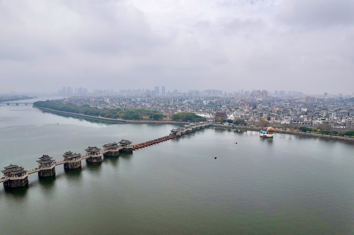 这是一张城市景观照片，图片展示了湖泊上的古桥和城市的天际线，天空多云。