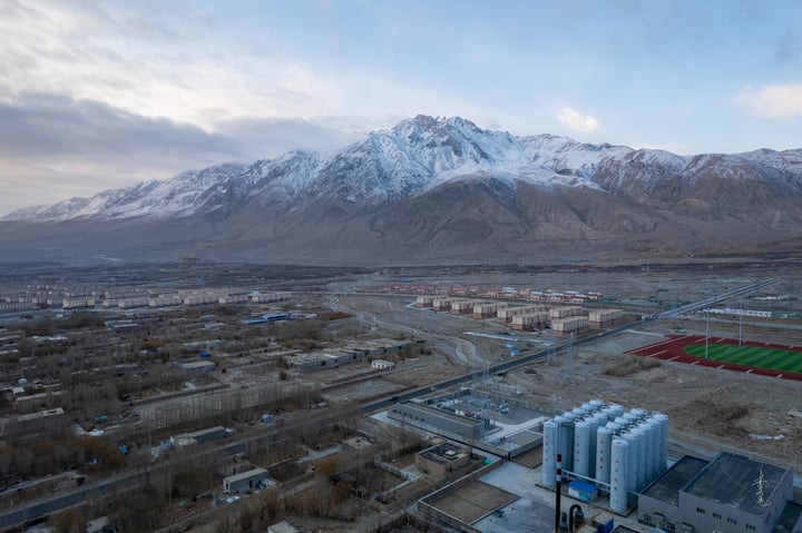 A panoramic view of a snow-capped mountain range, with a cityscape in the foreground, surrounded by trees and buildings.