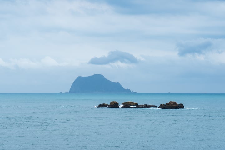 A serene ocean scene with a small island, rocks, and a cloudy sky.