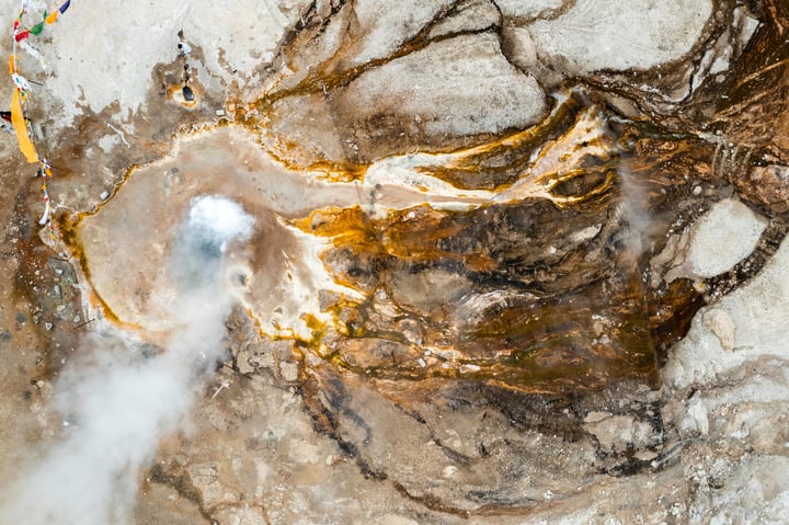 An aerial view of a rocky landscape with a large hole in the center, surrounded by a mix of brown and white rocks, and a small yellow cloud in the top right corner.