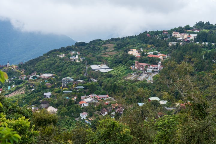 A mountainous area with houses, trees, and a cloudy sky.