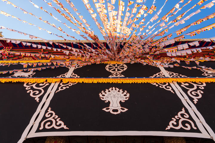 A close-up view of a temple with a black and white patterned roof adorned with colorful streamers, set against a clear blue sky.