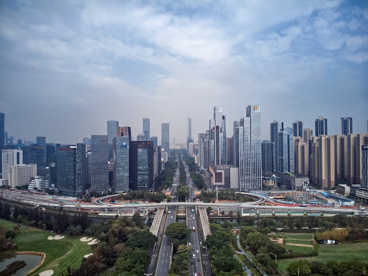 A bustling cityscape with towering skyscrapers, a highway, and a park, surrounded by greenery.
