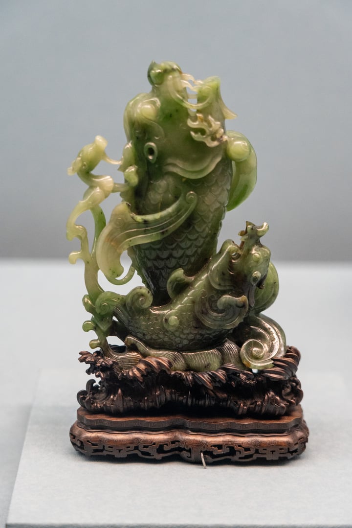 A green ceramic sculpture of a man and a dragon on a pedestal, with intricate details and a golden dragon on the man's head.