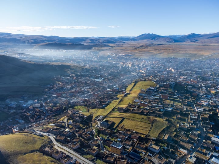 An aerial view of a city nestled between mountains, with a mix of buildings and green spaces, surrounded by snow-capped mountains.