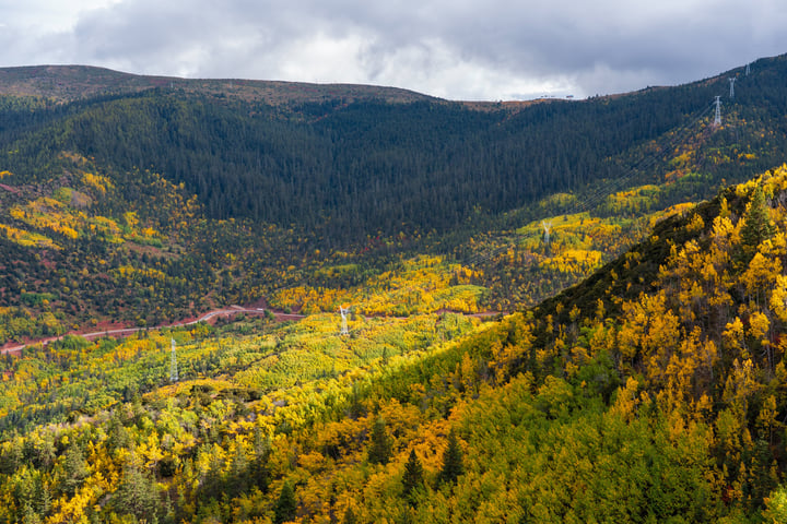 A mountain range with a red river winding through it, surrounded by trees in autumn colors, with a white waterfall in the distance.