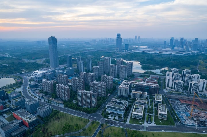 An aerial view of a city with tall buildings, a river, and a park, with a blue sky and clouds.