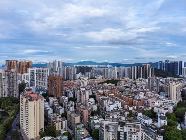 A panoramic view of a bustling city with tall buildings, a large body of water, and mountains in the background.