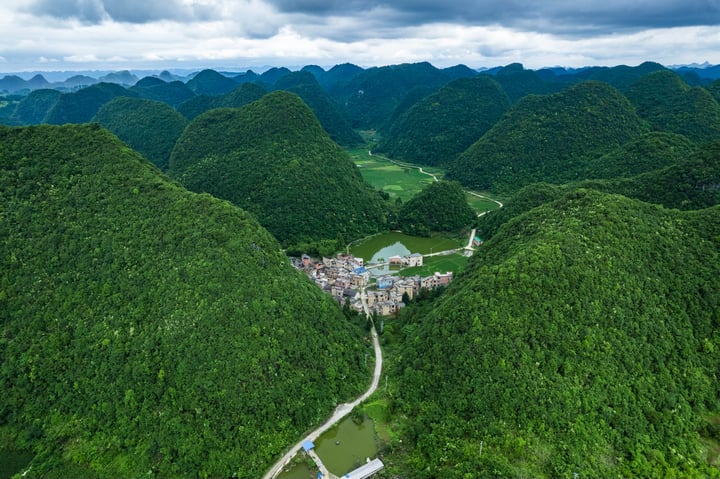An aerial view of a mountainous landscape with a small town nestled amidst verdant hills and mountains, surrounded by a cloudy sky.