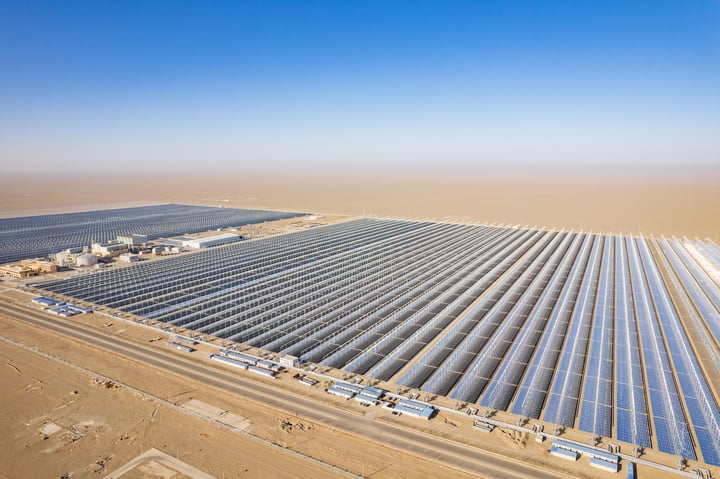 An aerial view of a large solar farm with rows of solar panels in a desert-like environment.