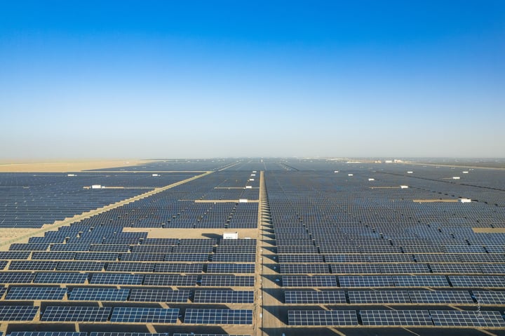 An aerial view of a large solar farm with rows of solar panels in a desert-like environment.