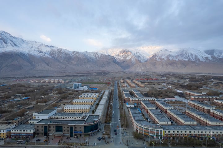 A panoramic view of a snow-capped mountain range, with a cityscape in the foreground, surrounded by trees and buildings.