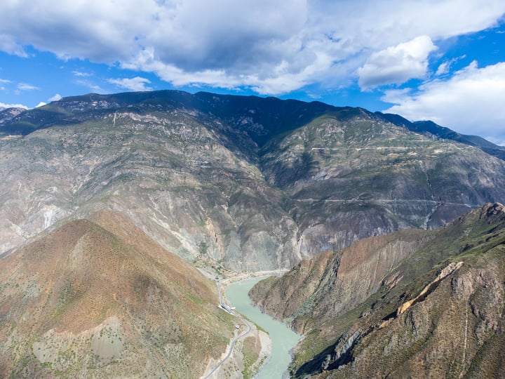 A breathtaking view of a valley with a river winding through it, surrounded by mountains and a blue sky with clouds.