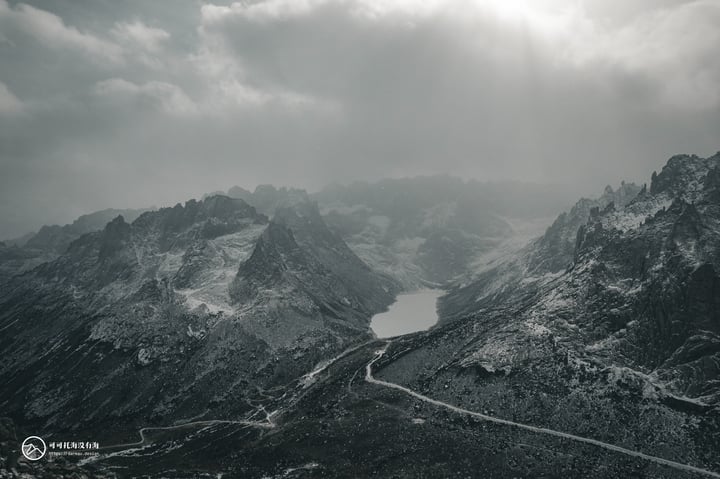 A mountain range with snow-covered peaks and a lake in the middle, with a road winding through the landscape.