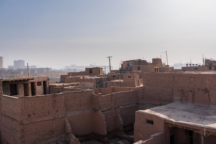 A cityscape with old brick buildings, a hazy sky, and a few tall buildings in the distance.