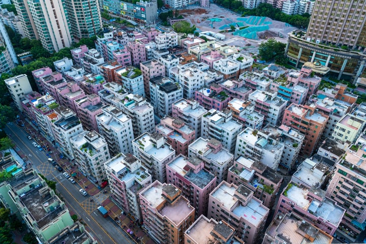 An aerial view of a densely packed city with a mix of residential and commercial buildings, some with green roofs, surrounded by roads and cars.