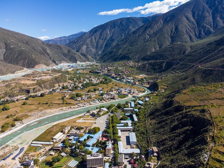 An aerial view of a mountainous valley with a winding river, surrounded by lush greenery and mountains, showcasing a harmonious blend of nature and human habitation.
