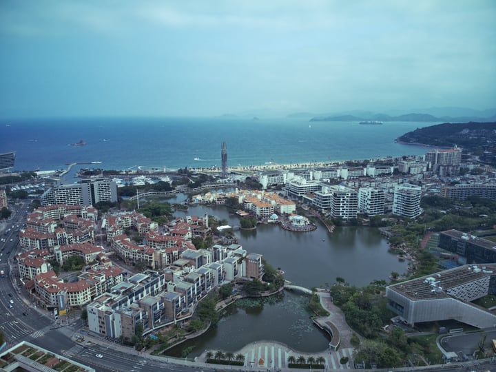 An aerial view of a city with a large body of water, a bridge, and a lighthouse, surrounded by mountains and a large body of water.