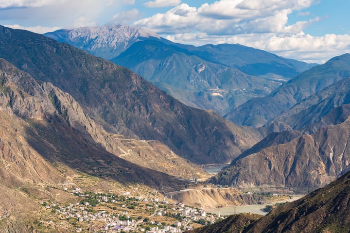 A breathtaking mountainous landscape with a winding river, a small town, and a clear blue sky with white clouds.