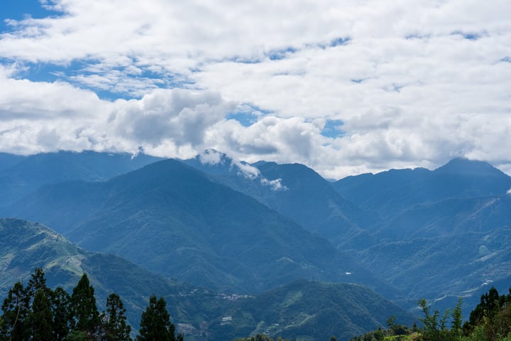A breathtaking mountainous landscape with lush greenery and a clear blue sky with fluffy white clouds.