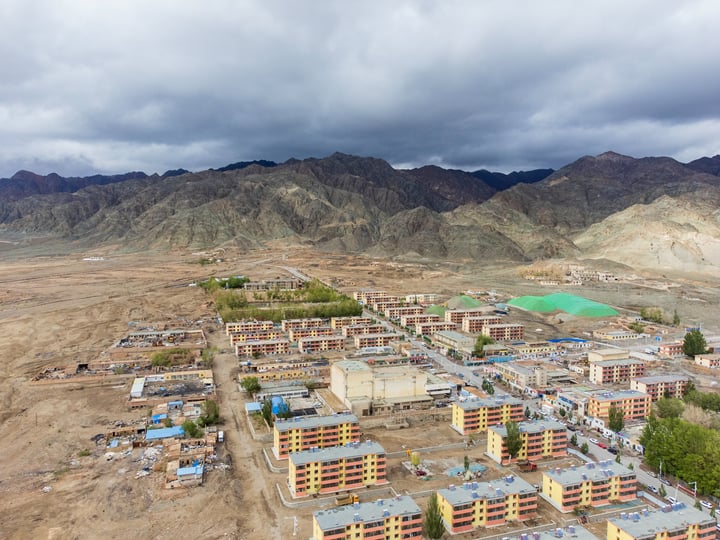An aerial view of a mountainous area with a large city in the center, surrounded by mountains and a green field.
